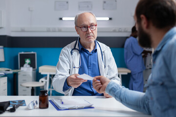 Physician giving prescription file to ill patient at checkup visit. General practitioner preparing treatment and medicine for man with disease, after medical examination in cabinet.