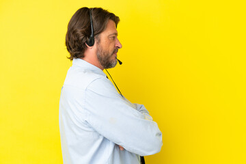 Telemarketer dutch man working with a headset isolated on yellow background in lateral position