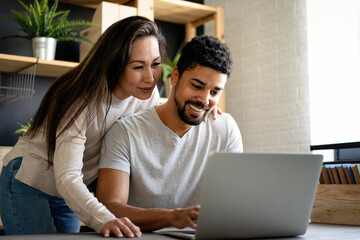 Happy interracial couple smiling while working or having fun at laptop