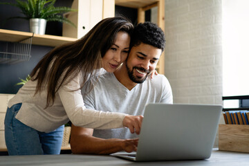 Happy interracial couple smiling while working or having fun at laptop