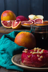 dessert Bloody Sicilian oranges on wooden table, tea and donut covered with red icing with pine nuts