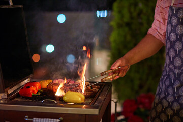 a man is grilling the food, vegetables and steaks on bbq on the patio at summer evening