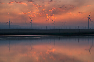 Fototapeta na wymiar Windmill turbines at sunrise with reflection