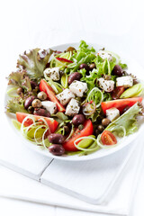 Healthy salad with feta cheese, various olives, leek and tomatoes. White wooden background. Close up.