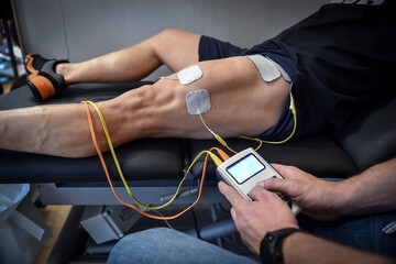 Muscle stimulator device with electrodes applied to quadriceps by a professional physiotherapist - Powered by Adobe
