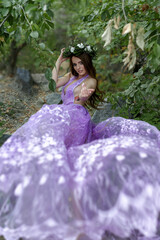 Mavka water nymph naiad near the water in nature in the forest on the river bank of the lake on a quarry on a cliff in a purple lilac transparent dress with a wreath on her head