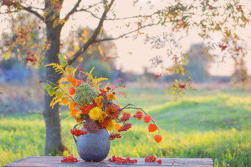 bouquet autumn flowers in rustic jug on wooden table outdoor at sunset