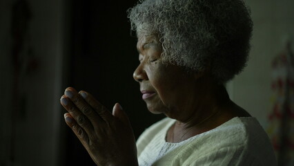 Pensive senior woman praying with eyes closed at home