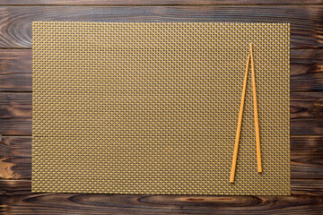 Two chopsticks and bamboo mat on wooden background. Top view, copy space