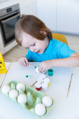 Easter, a little boy happily painting eggs, in front of him is a homemade bunny made of paper