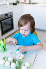 Easter, a little boy happily painting eggs, in front of him is a homemade bunny made of paper