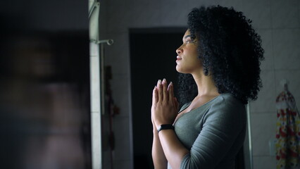 An African woman praying to God standing at home by window