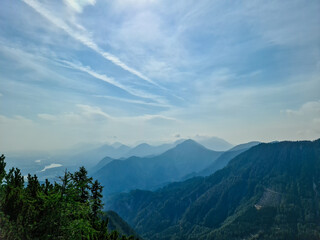 Scenic view on the alpine mountain chains of the Karawanks in Carinthia, Austria. Peaks are shrouded in morning fog. Mystical vibes. Clear and sunny day.  Serenity. View from Ferlacher Spitze, Alps