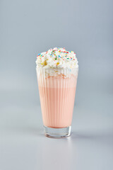 Pink milkshake with whipped cream and colored sugar sprinkles on gray background