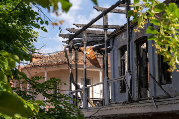 partially burned house between green tree branches on a sunny day.
