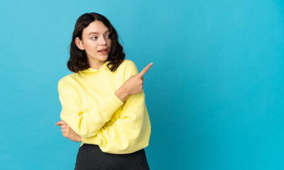 Teenager Ukrainian girl isolated on blue background surprised and pointing side