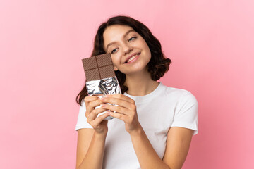Teenager Ukrainian girl isolated on pink background taking a chocolate tablet and happy