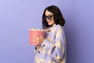 Teenager Ukrainian girl isolated on purple background with 3d glasses and holding a big bucket of popcorns