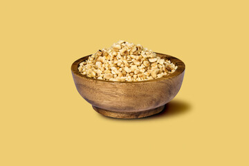 Olive in wooden bowl and scattered hazelnuts, isolated on yellow background with reflection.