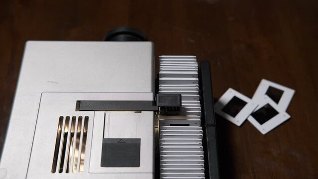 Slide magazine projector in operation. Top view of antique white slider projector working to project slide photographs and to create slideshow. Thin-film slides in a white plastic frame. Vintage produ