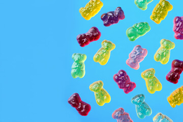 Multicolored flying gummy bears on blue background, flat lay