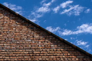 a large old brick part of the roof of a building that forms a triangle dividing the picture into two parts where there is a beautiful blue sky with white clouds