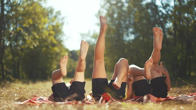 kid playing in the park. a group of children lie on their backs swinging their legs. happy family kid dream concept. fun happy family kids raised their feet up on nature in the park
