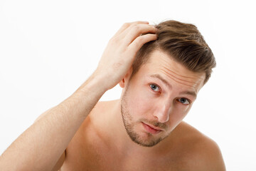 A young man looks at himself in the mirror, his hair began to fall out early.