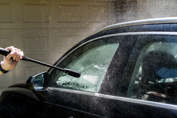 Selective focus shot of washing a black Suv 4wd car with high pressure washer cleaner. Car wash
