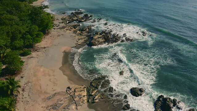 Aerial view over waves hitting rocks at the Playa Mal Pa&iacute;s beach, in sunny Costa Rica - tilt, drone shot