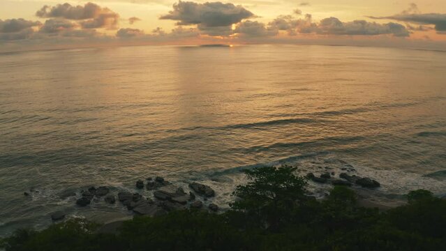 Aerial view over waves hitting rocks at the Playa Mal Pa&iacute;s beach, sunset in Costa Rica - tilt, drone shot