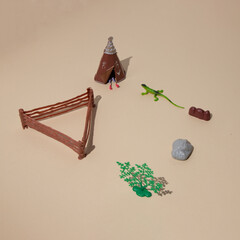 An Indian wigwam with legs protruding from it, a lizard, a barn and a tree in the desert with copy space. Minimal nomad scene.