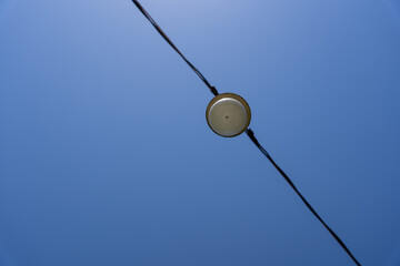 a blue sky whose black electric cable with a lantern divides it diagonally into two parts.