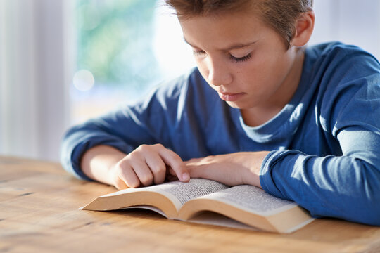 Hes really getting into this book. Shot of a young boy reading a book at a table.