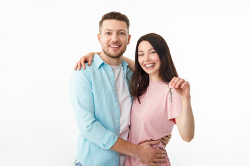 Fototapeta premium A cheerful young couple is hugging in the kitchen, holding the keys to a new house in their hands. Happy newlyweds moved into a new apartment, got a mortgage, moving day.