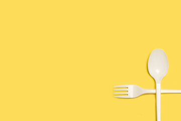 Tenedor y cuchara cruzados de plástico blanco sobre un fondo amarillo liso y aislado. Vista superior. Copy space