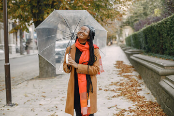 Young black woman in a coat standing under a transparent umbrella outside