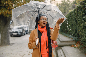 Young black woman in a coat standing under a transparent umbrella outside