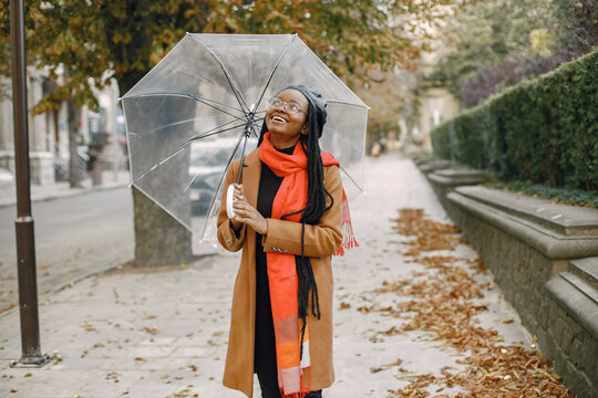 Young Black Woman In A Coat Standing Under A Transparent Umbrella Outside