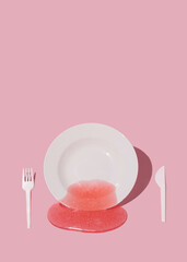 White plate with slime, fork and spoon on a pastel pink background. Abstract meal and diet concept with copy space.