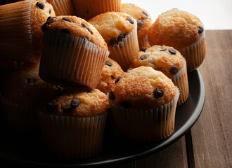 Close up or macro photography, vanilla cupcakes with chocolate chips on a white plate over a wooden lit by a window light. concept of homemade sweet bread. Horizontal