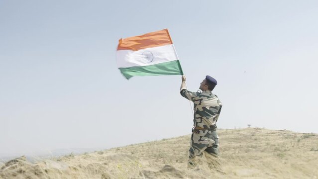 full shot Indian army soldier holding waving Indian flag on top of mountain - concept of independence or repubilc day celebration, patriotisms and freedom