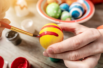 Hand with a brush is drawing a colored pattern on an Easter egg. Preparation for the bright Easter holiday