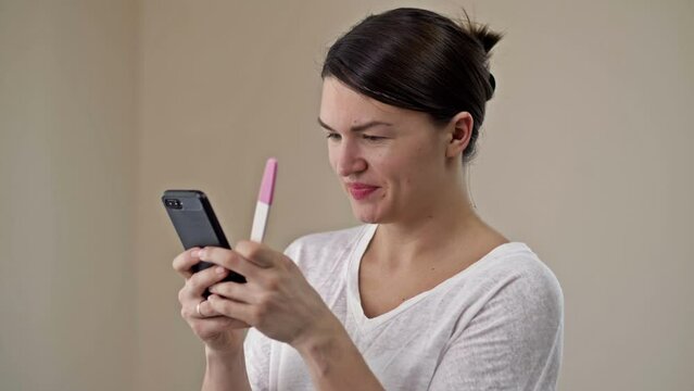 Young woman is happy to see a positive pregnancy test. She hurries to share her joy on the phone with a loved one.