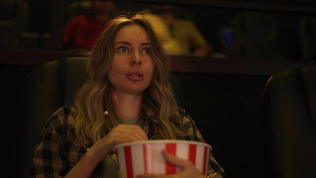 Woman sitting in armchair watching a horror movie at the cinema, scatters the popcorn from fear