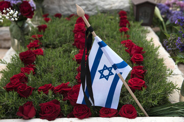 A flag of the State of Israel rests on a grave of a fallen soldier covered with colorful flowers in...
