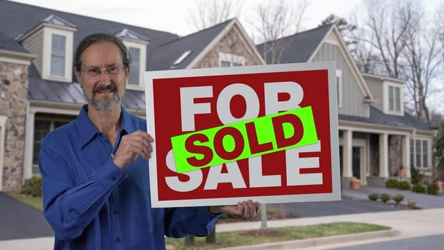 Happy smiling real estate agent holding SOLD sign in front of a house.