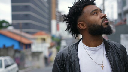 A pensive African American man looking up to sky in contemplation standing by urban street