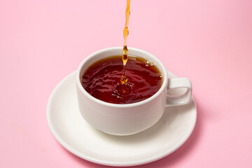 Tea is poured into a cup of tea on a pink background. Pour fresh tea. Invigorating and tonic tea drink.