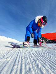 The girl fastens the snowboard fastenings. A snowboarder girl in the snowy mountains, sitting on...